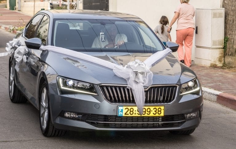 סקודה אפור כהה עם צלב סרט לבן גדול על מכסה המנוע ופרחים לבנים