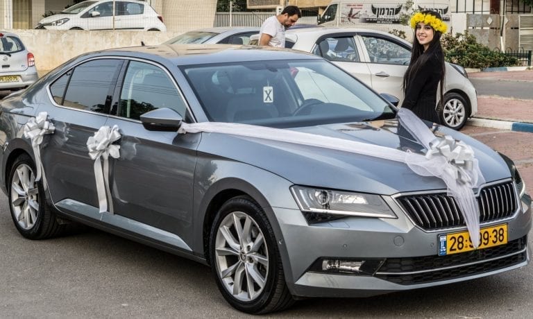 כלה מחייכת ליד רכב מקושט בסרט טול לבן לפני החופה – קישוט רכב כלה ברחובות